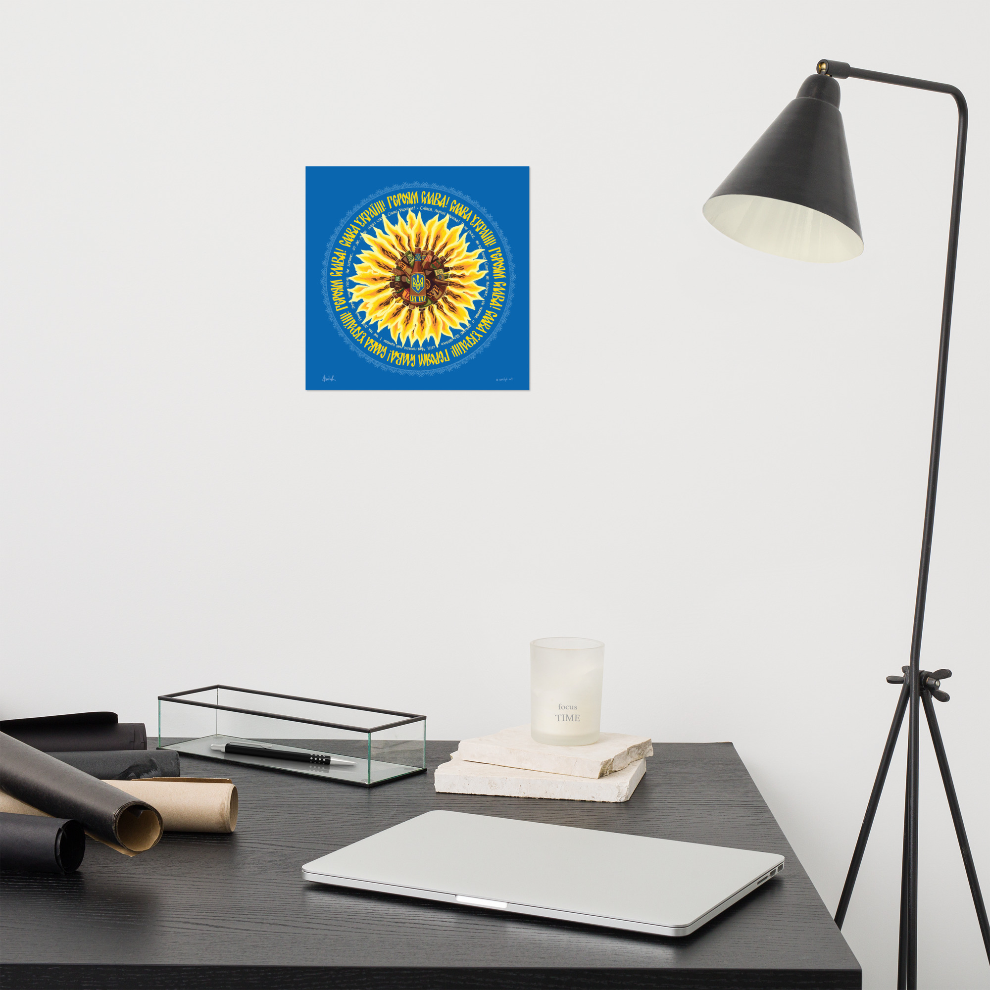 Square print on a wall above a desk. There is also a studio lamp to the right.