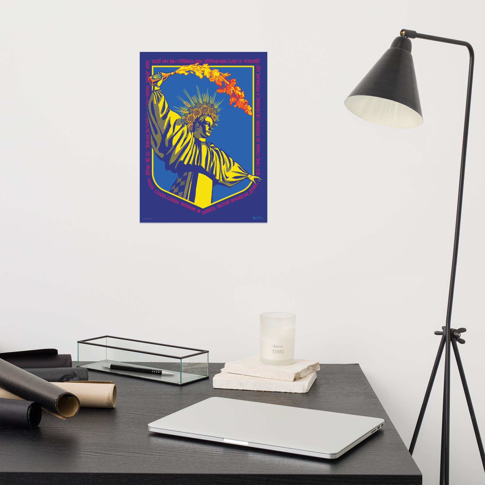 The print hangs on a wall above a busy desk. There is a studio lamp to the right.